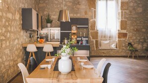 Comedor con mesa de madera, sillas blancas, un florero con plantas y pared de piedra de fondo.