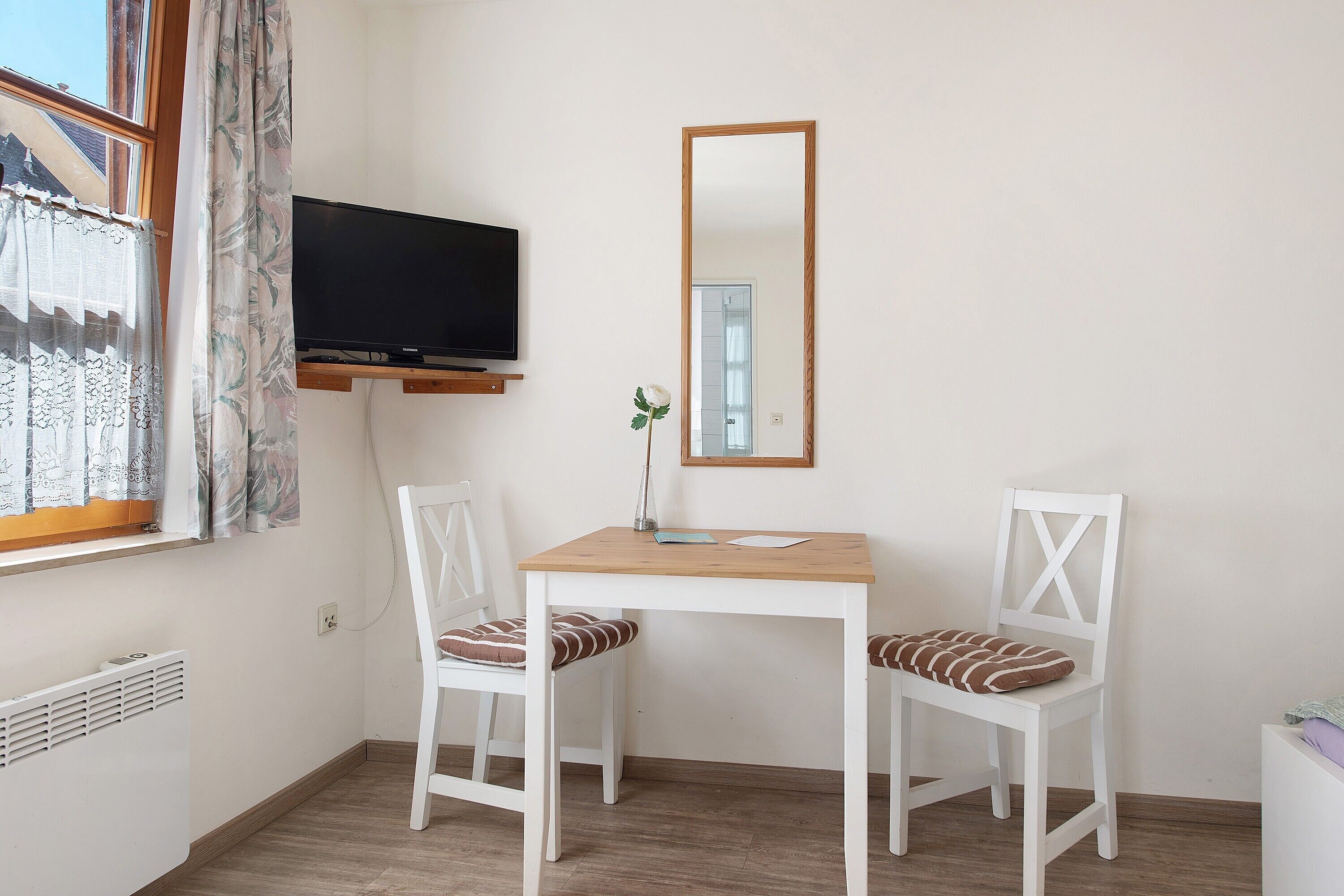 A small room with a wooden table, two white chairs, a television, and a mirror.