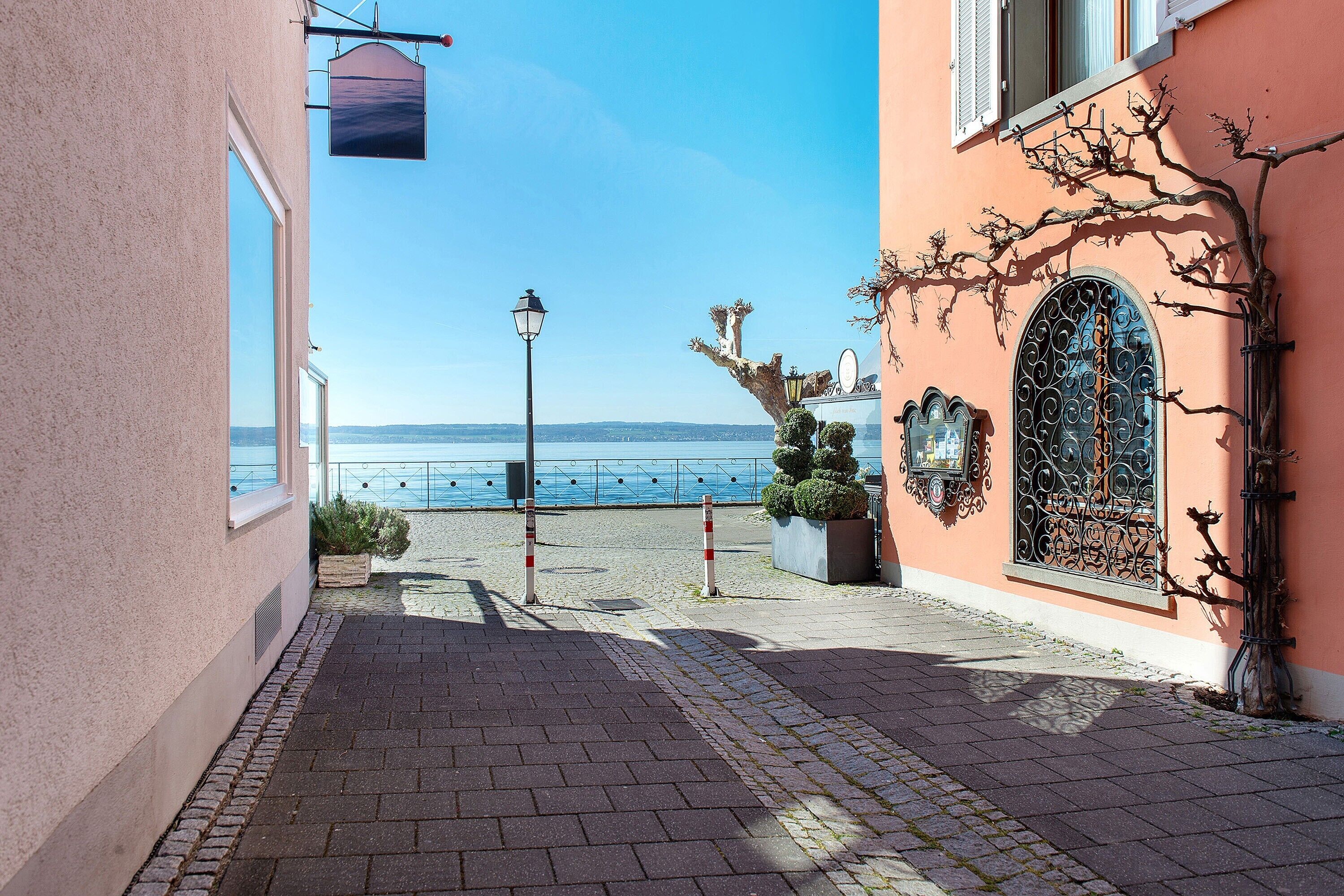 A coastal street with a paved walkway, a lamp post, and a building with a decorative iron gate and window.