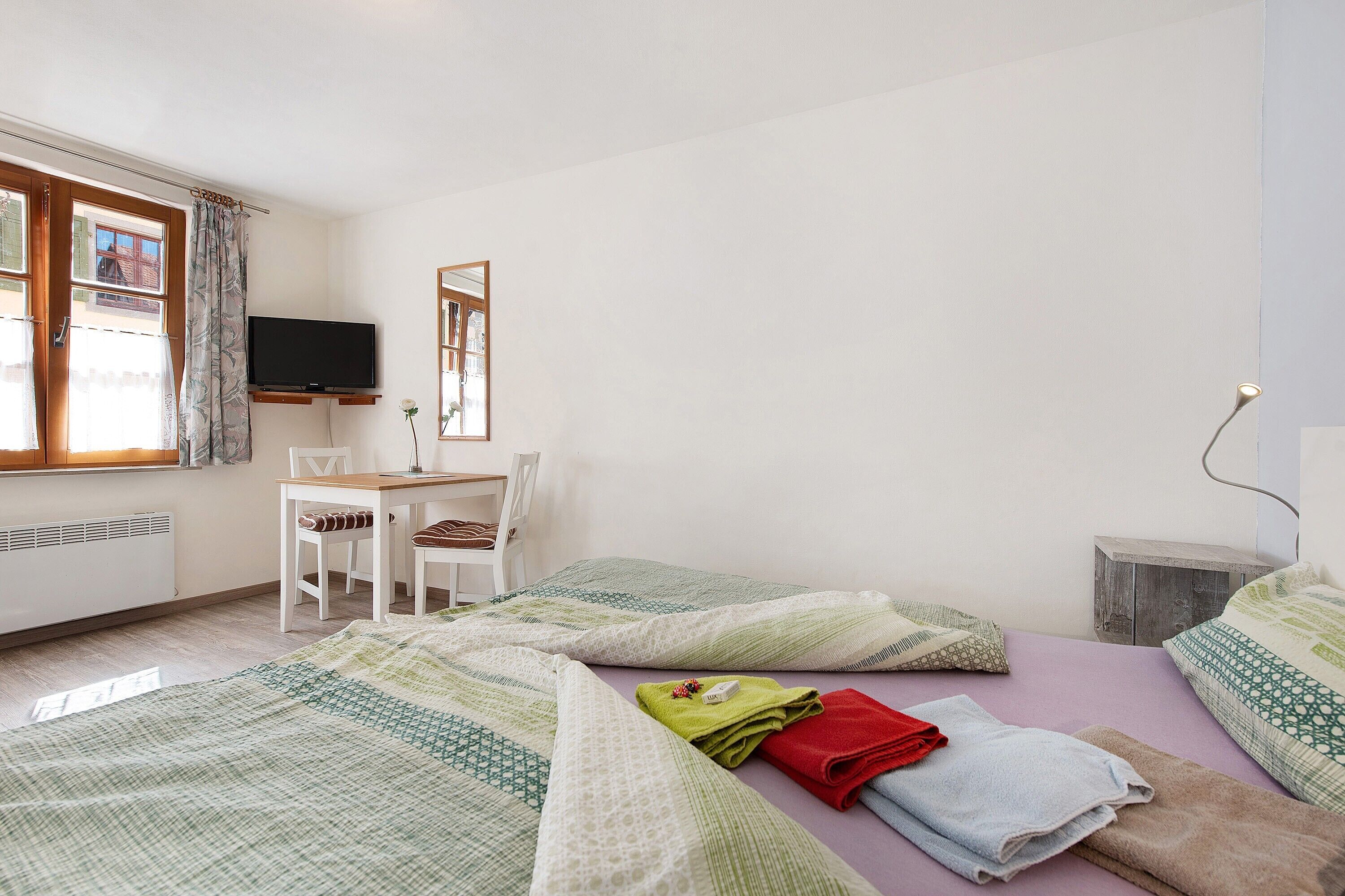 Ein Schlafzimmer mit zwei Betten, einem Schreibtisch, einem Stuhl, einem Fernseher und einem Fenster mit Vorhängen.