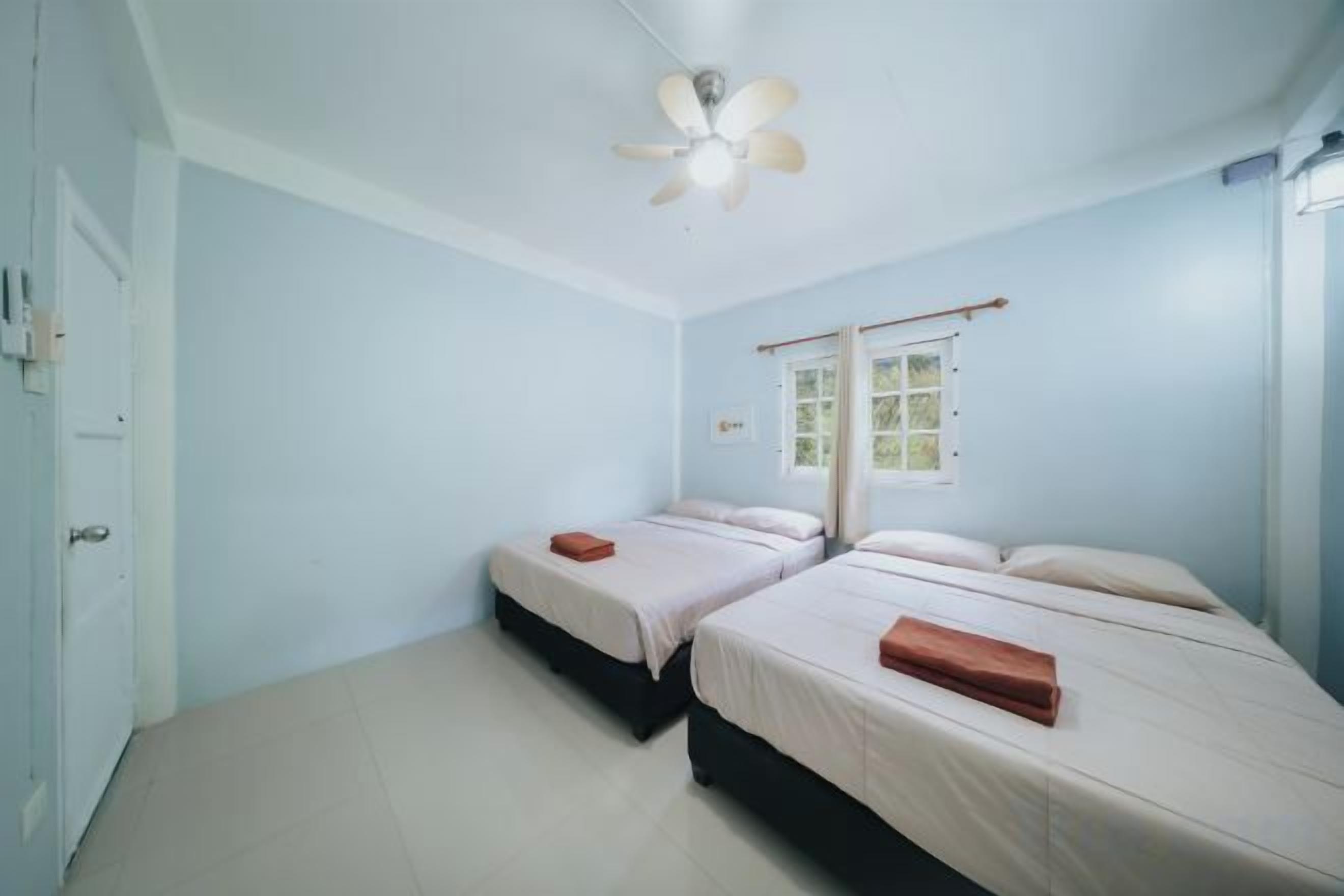 A room with two beds, a ceiling fan, and a window with a view.