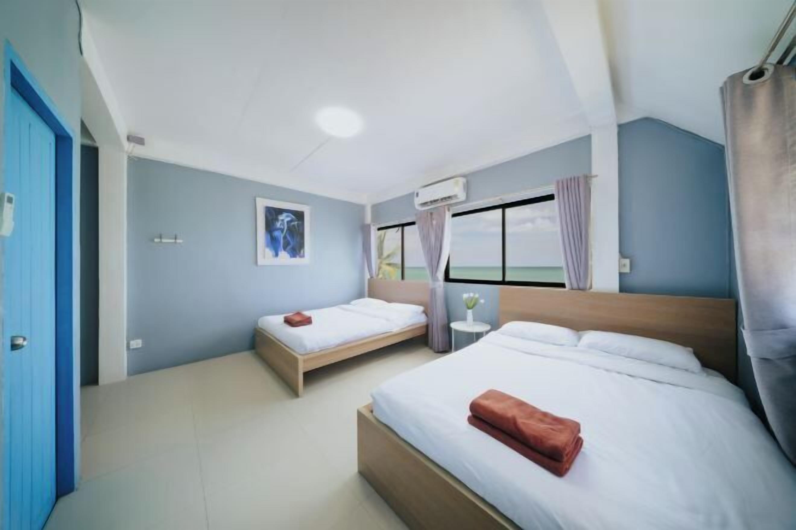 Habitación de hotel con dos camas, una ventana con cortinas, un ventilador de techo y aire acondicionado instalado en la pared.