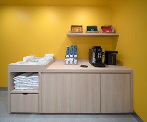 Un espace d’accueil d’hôtel comprenant un comptoir, une machine à café et un espace de rangement pour les serviettes et les articles de toilette.