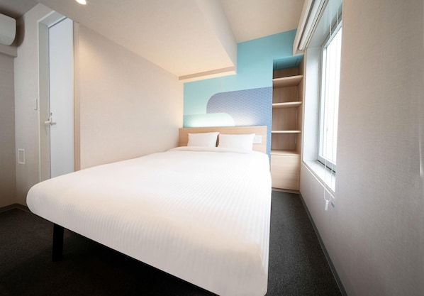 A hotel room with a bed, a wardrobe, a window, and a wall with a geometric pattern.