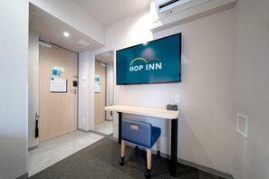 Un pasillo de hotel con una recepción, un cartel en la pared que dice 'HOP INN' y un carrito azul pequeño.