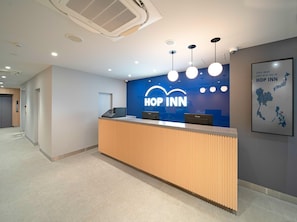 A reception desk with a blue wall and the 'HOP INN' logo, a modern design with pendant lighting, and a map of Japan on the wall.