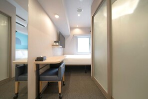 Habitación de hotel pequeña con cama, escritorio, silla, ventana y televisión de pantalla plana.