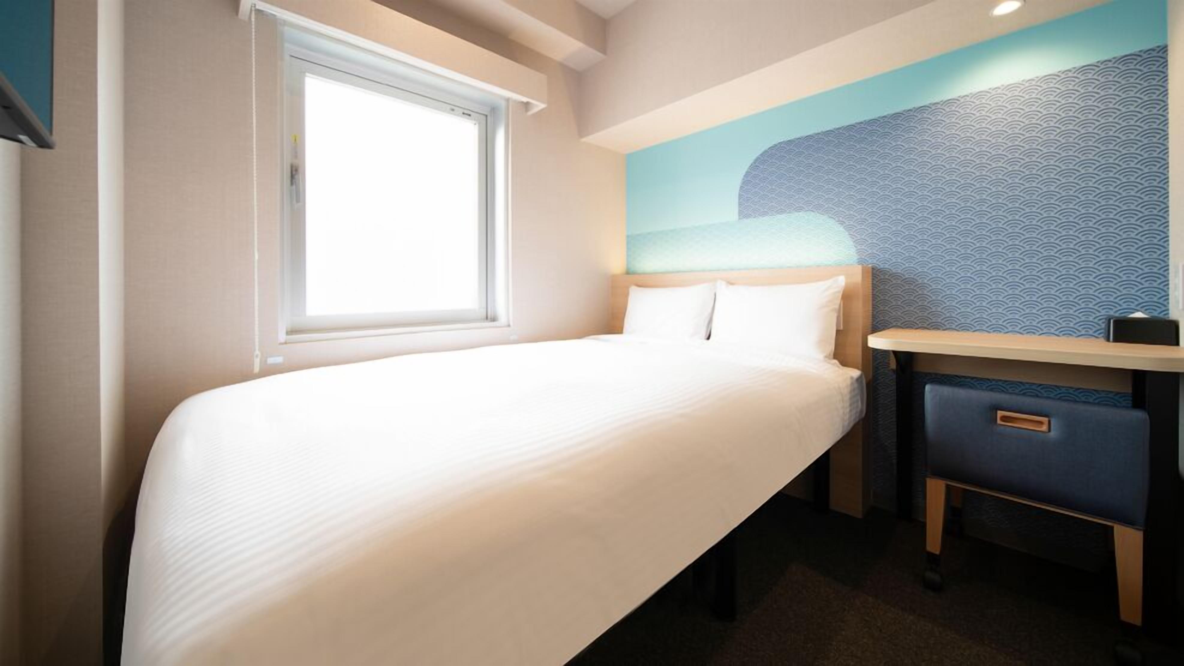 A hotel room with a bed, a desk, and a window.
