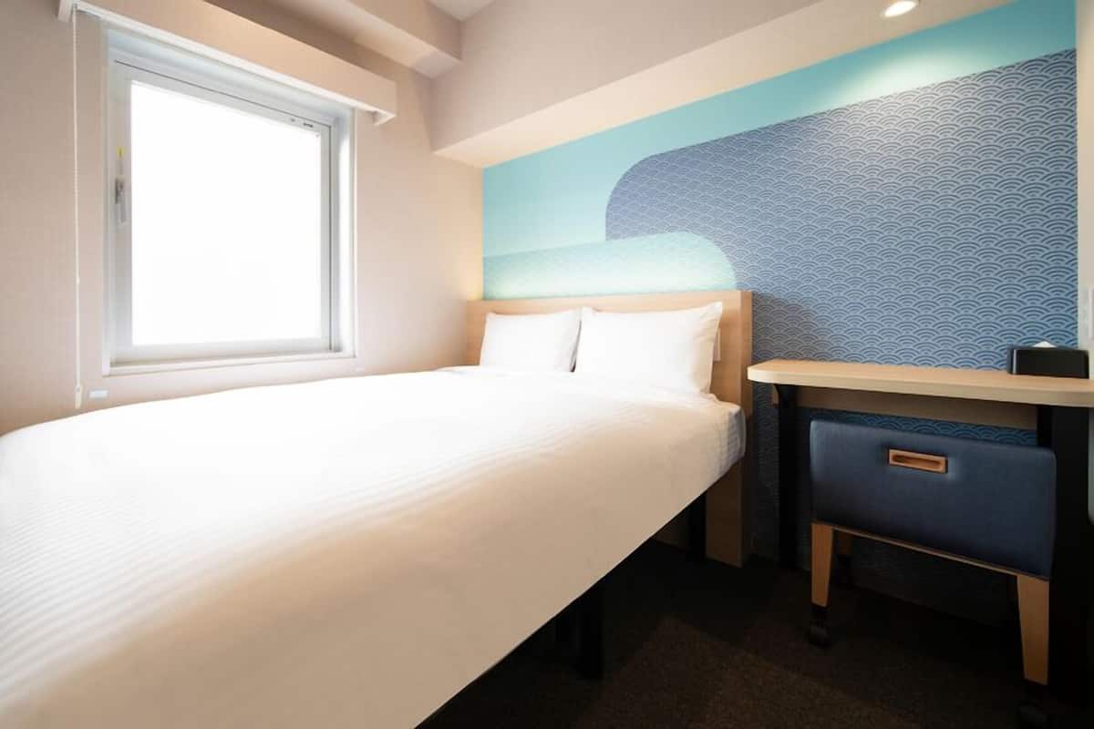 A hotel room with a bed, a desk, and a window.