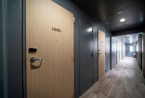 Un couloir avec des portes numérotées 1001 et 1002, un plancher en bois et un extincteur sur le côté droit.
