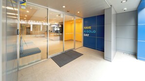 A modern hotel entrance with glass doors, a reception desk, and a blue wall with 'HAVE A GOOD DAY' signage. - Hop Inn Tokyo Ueno (Tokyo)
