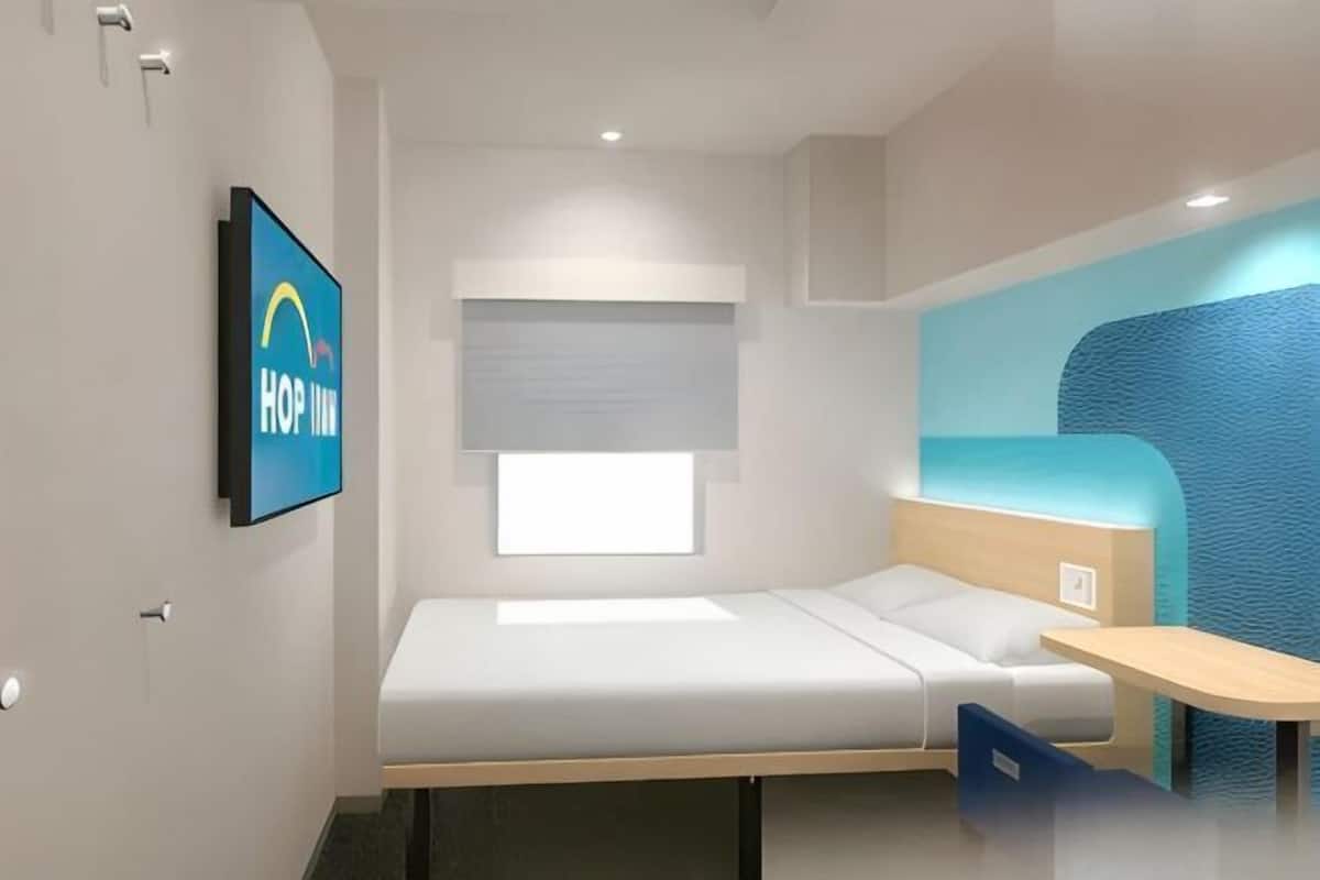 A compact room with a bed, a small table, a chair, a TV, and a window.