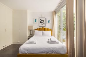 Une chambre d’hôtel moderne avec un grand lit, une table de chevet, une commode et une fenêtre avec des rideaux.