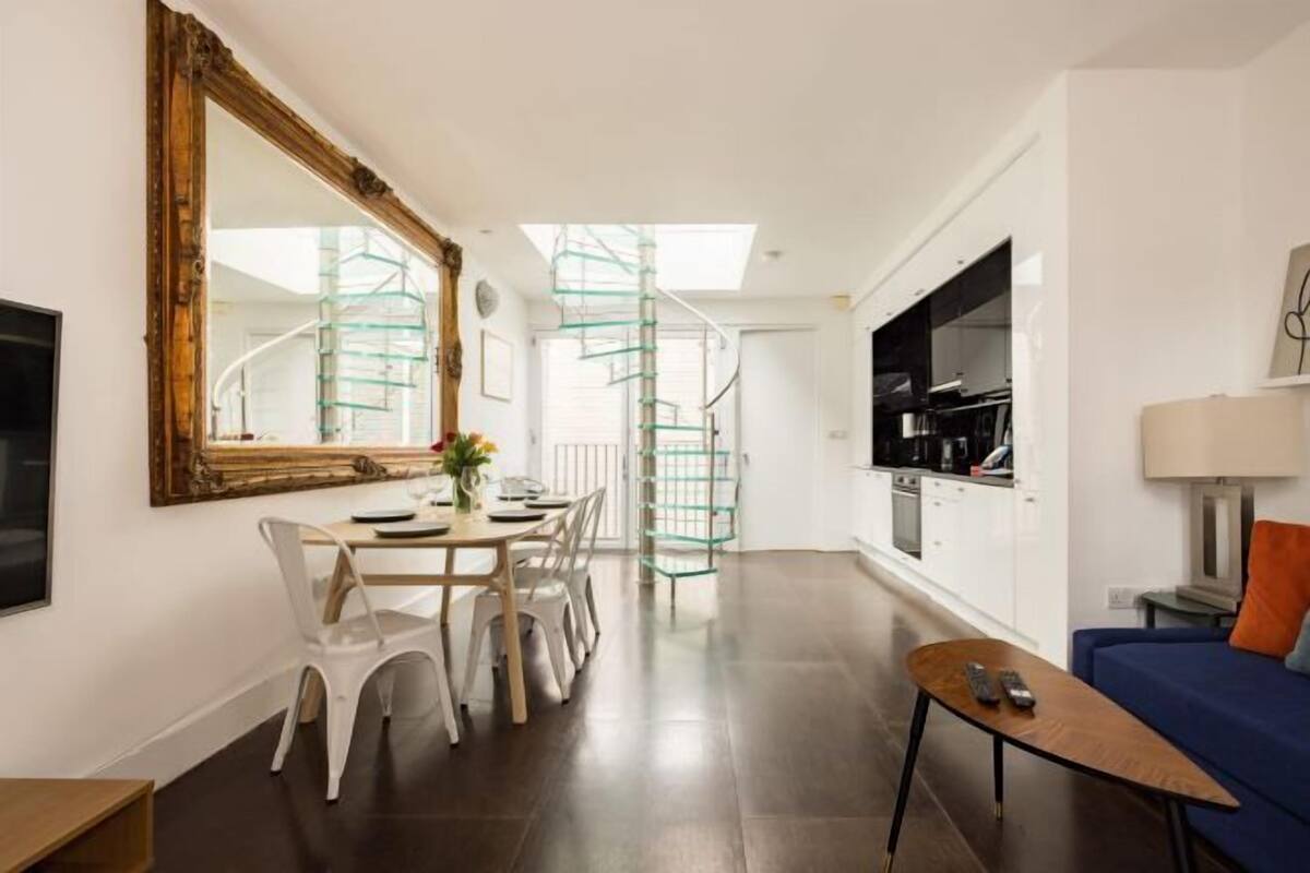 A modern apartment with a dining area, a sofa, a TV, and a staircase.