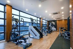 Un gimnasio con diversos equipos de ejercicio, amplias ventanas y vistas de la ciudad.