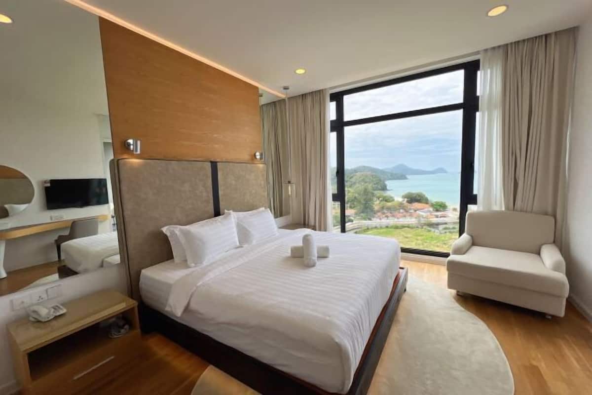 A hotel room with a large bed, a sofa, a desk, and a view of the sea.