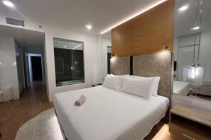 Ein modernes Hotelzimmer mit einem großen Bett, einem Holz-Kopfbrett, einem Nachttisch, einem Spiegel und einem Fenster mit Vorhängen.