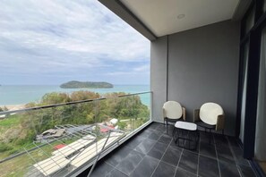 Un balcon avec vue sur la mer et une île, deux chaises blanches et une petite table.