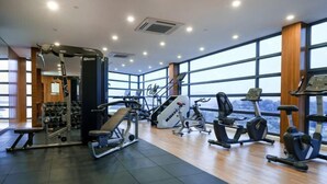 Un gimnasio con equipos de ejercicio variados, amplias ventanas y vistas a la ciudad.