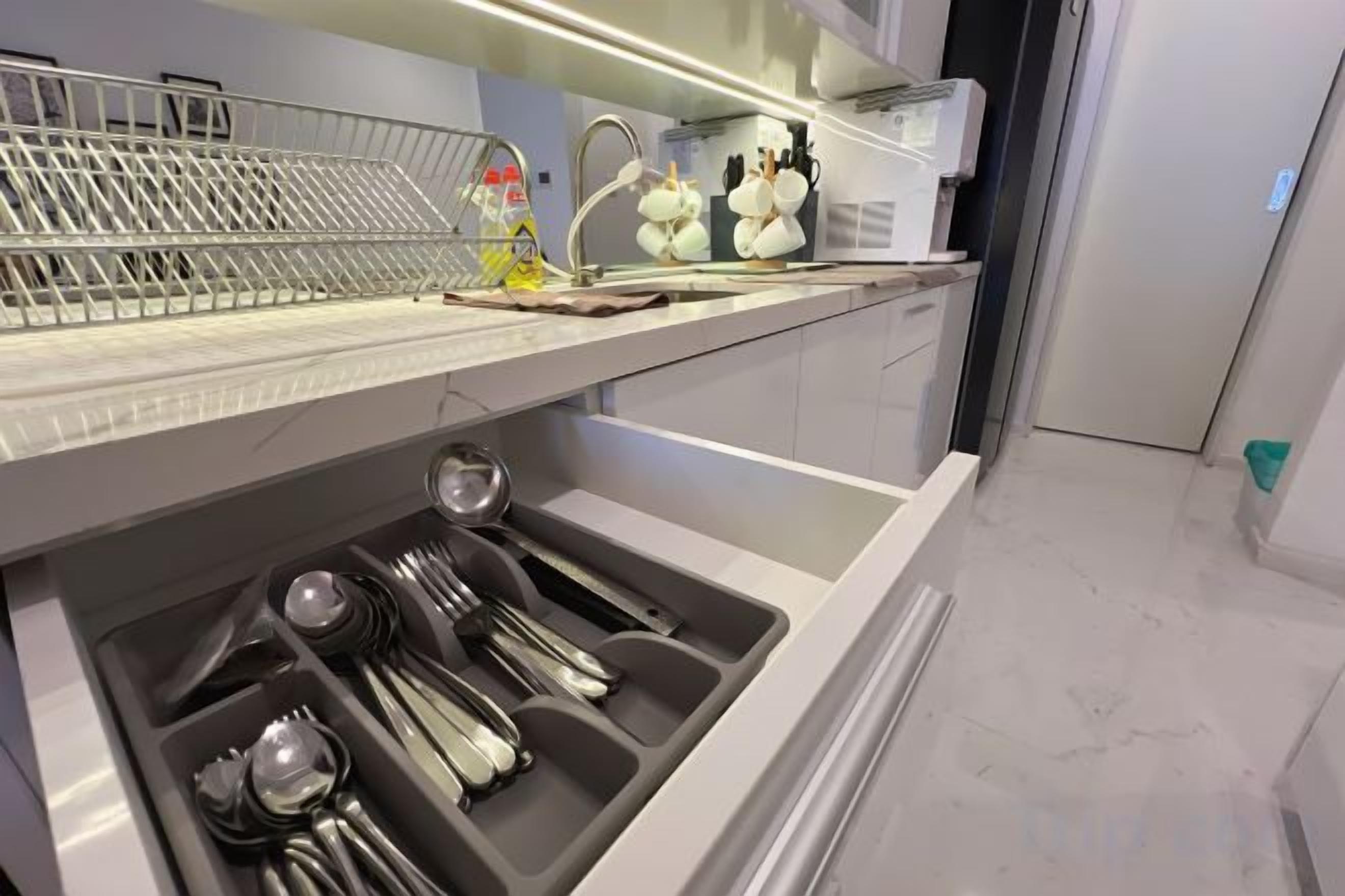 A modern kitchen with a built-in sink, a dish rack, and a drawer with utensils.