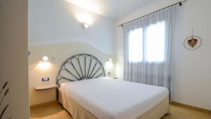 Un dormitorio con cama, dos mesitas de noche, una lámpara de pared, una ventana con cortinas y un adorno en la pared.
