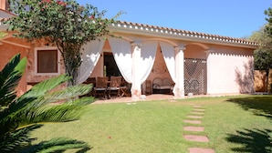 Una casa con patio, zona de estar techada y jardín con una palmera.