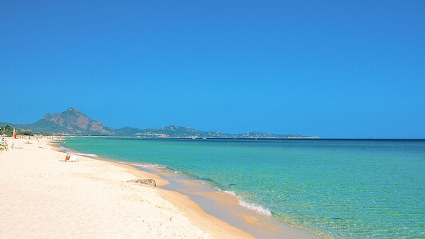 Una playa con agua turquesa cristalina, una orilla arenosa y una montaña al fondo.