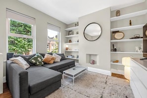 A modern living room with a grey sofa, a coffee table, and built-in shelving. - Unique 2 bedroom Flat in Heart of Walthamstow (Waltham Forest)