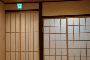 A traditional Japanese room with sliding doors, a green exit sign, and a wooden floor. - Haku Flower's Seven (Kyoto)