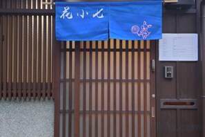 A wooden gate with a blue cloth hanging above it, a wooden wall with vertical slats, and a small electronic device on the wall. - Flower's Seven (Kyoto)