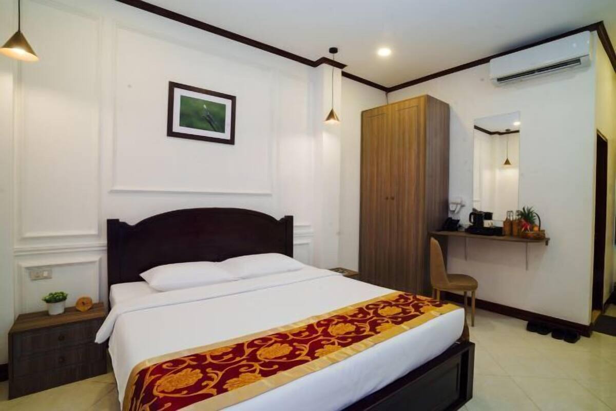 A hotel room with a bed, a wardrobe, a desk with a chair, and a mirror.