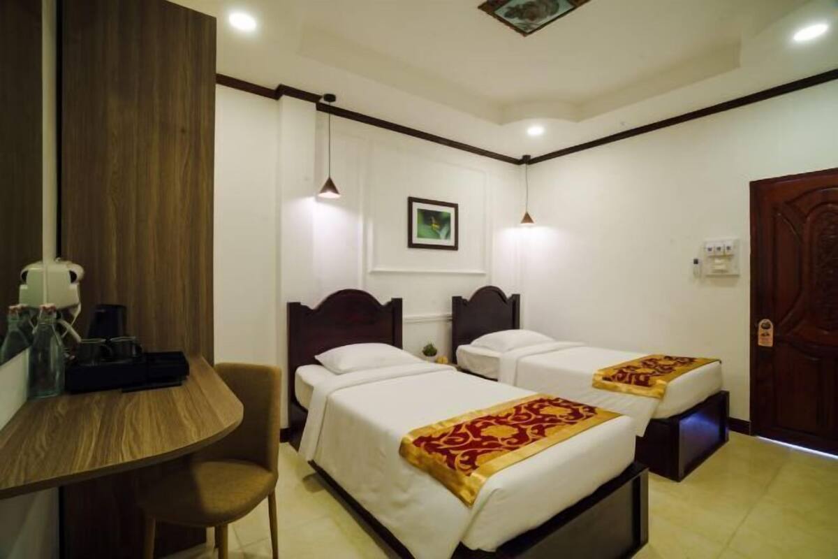 A hotel room with two beds, a wooden desk, and a chair.