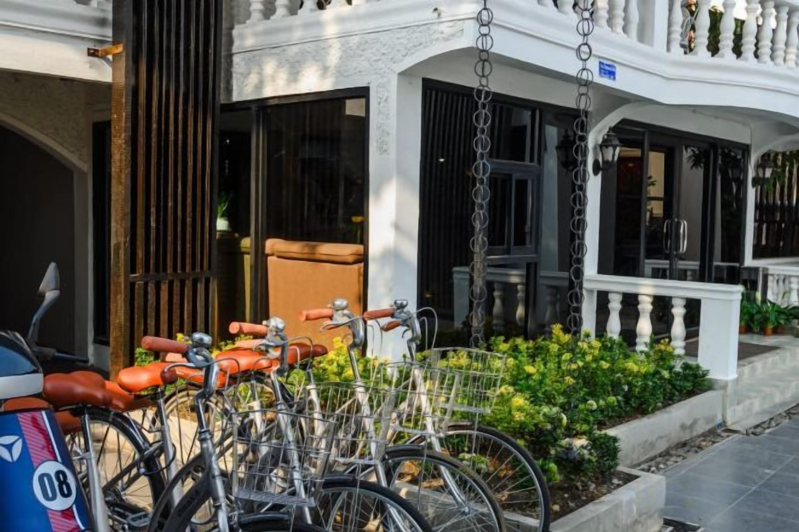 A row of bicycles parked outside a building with a white exterior and a balcony.