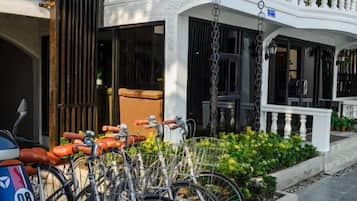 A row of bicycles parked outside a building with a white exterior and a balcony.