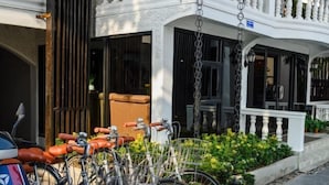 Ein Gebäude mit weißer Fassade, einer überdachten Veranda mit weißem Geländer und einem Fahrradständer mit mehreren Fahrrädern.