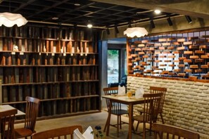 A cozy restaurant with a brick wall bookshelf, wooden tables, and chairs. - Hotel Lexi (Vientiane)