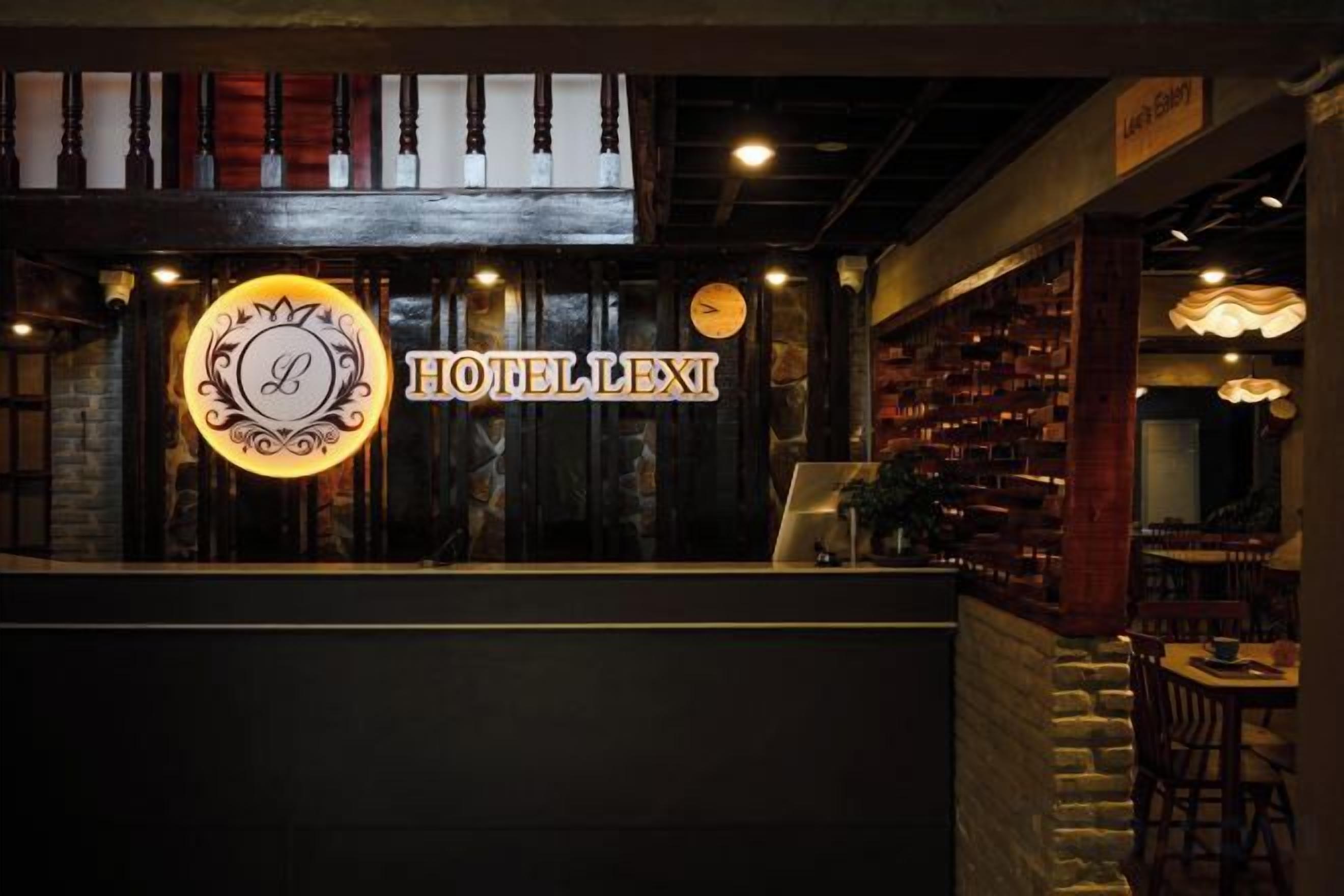 Een hotel receptie met een opvallend verlicht bord, houten inrichting en zithoekjes.
