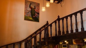 Eine Holztreppe mit dunkler Oberfläche, ein Pfau-Gemälde an der Wand und hängende Pendelleuchten.