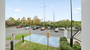 Un parking avec plusieurs voitures, un terrain de sport bleu et une vue sur des lignes électriques et des arbres.