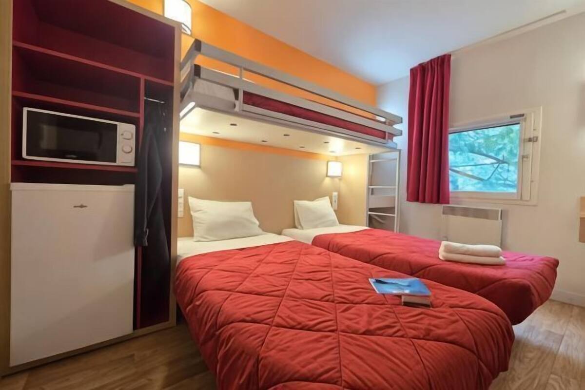 A compact hotel room with two beds, a microwave, a TV, and a small kitchenette.