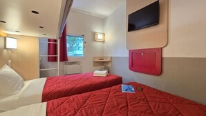 Une chambre d’hôtel avec deux lits, une télévision, une petite table et une fenêtre avec des rideaux.
