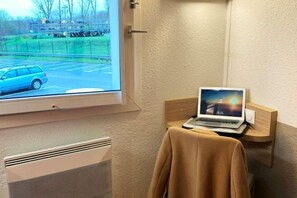 Una habitación con ventana que da a un estacionamiento, una computadora portátil sobre una estantería de madera y un radiador en la pared.