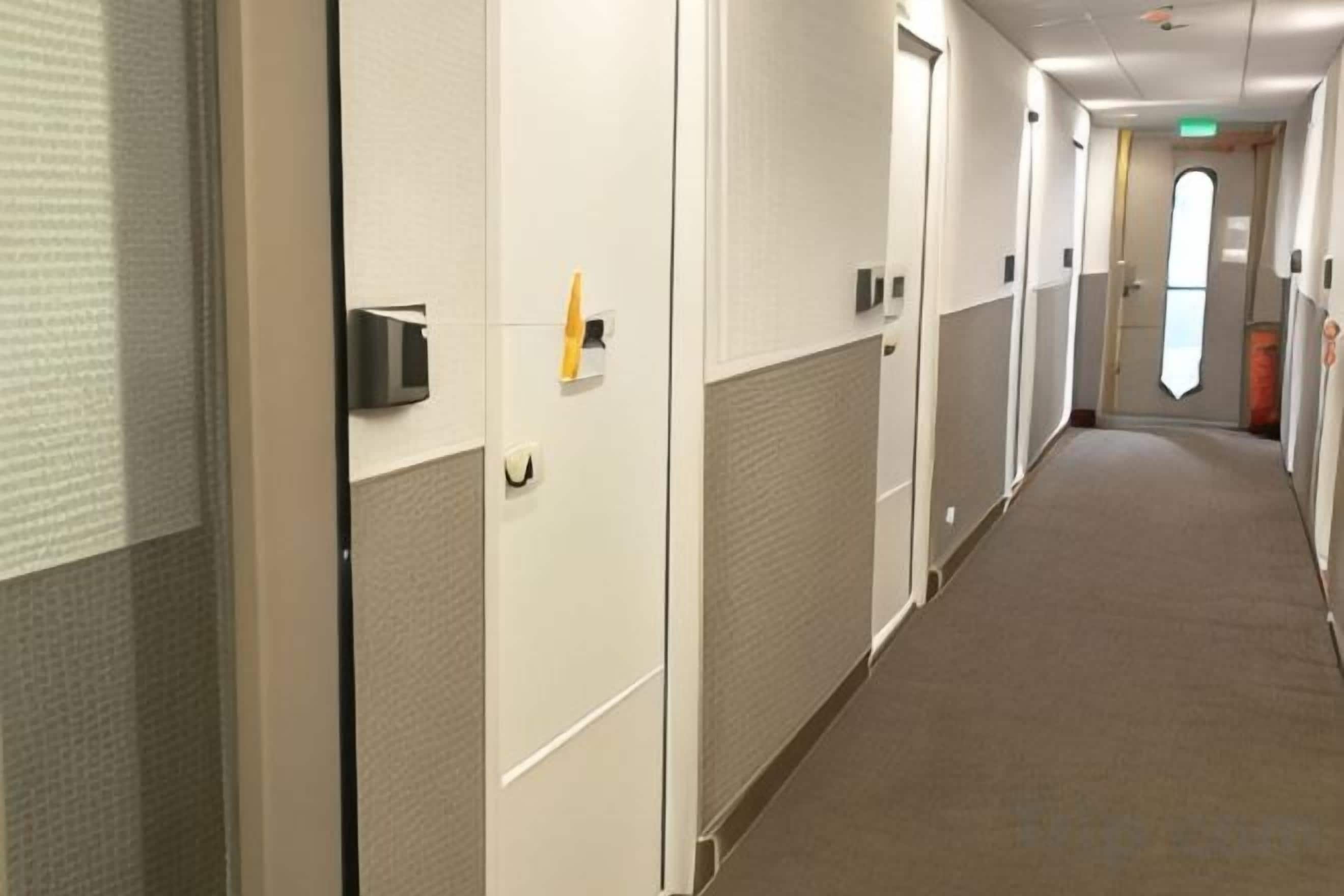 Un couloir avec des portes, une poubelle et une fenêtre au bout.