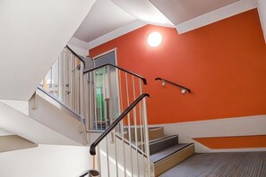 Una escalera con barandillas metálicas, una pared roja y un accesorio de iluminación en el techo.