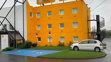 Un edificio amarillo con muchas ventanas y un coche blanco estacionado frente a él.