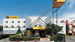 Un hôtel au design moderne, reconnaissable à son panneau « hôtel F1 » bien visible et à l’adresse de son site web, « hotelF1.com ».