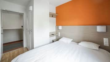 Une chambre d’hôtel comprenant un lit, une armoire, une table de chevet et un luminaire fixé au mur.