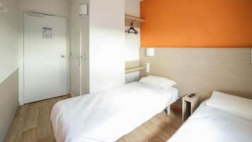 Een hotelkamer met twee eenpersoonsbedden, een houten vloer, een witte deur en een muur met oranje accent.
