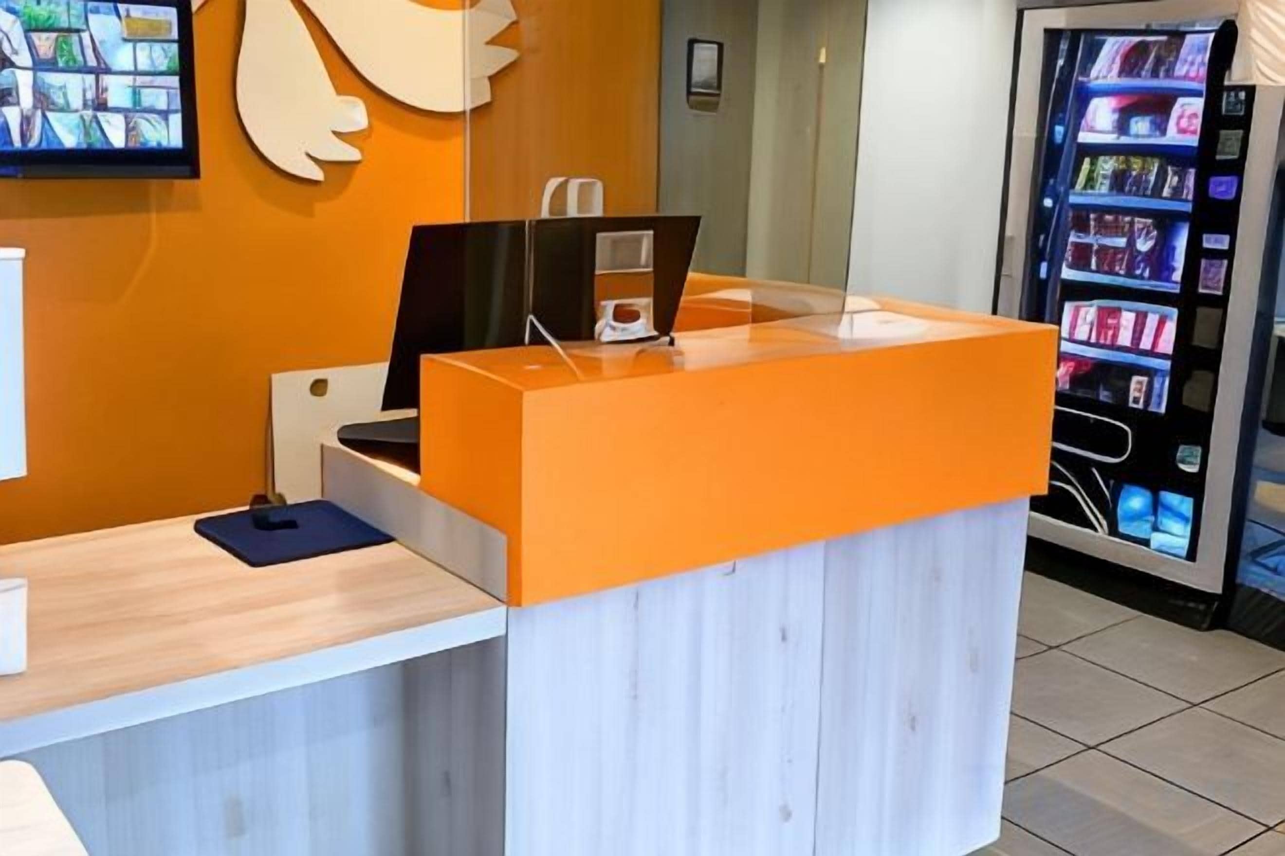 Een receptiebalie met een laptop, een automaat en een scherm aan de muur.