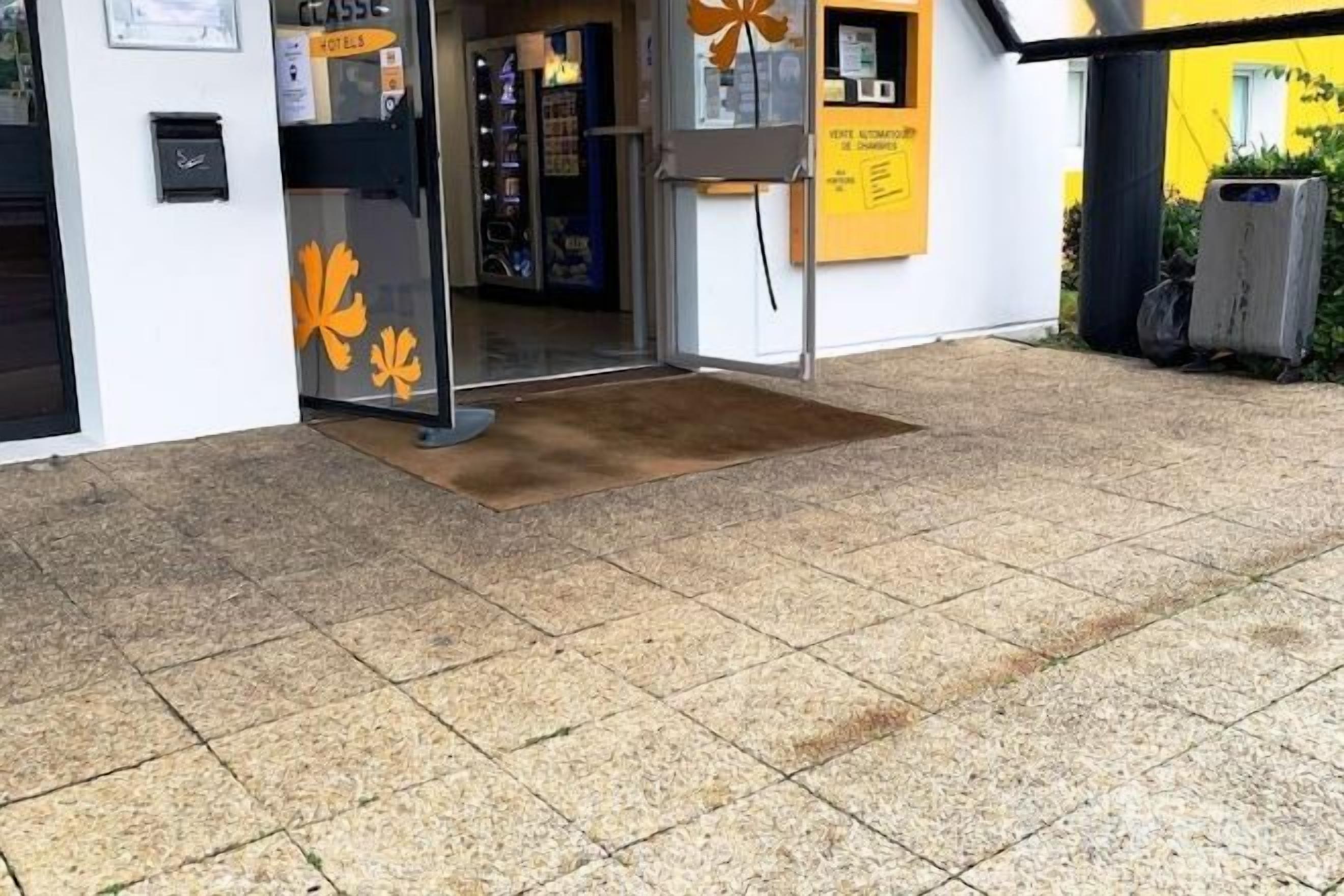 A building entrance with a tiled floor, a door with a leaf design, and a yellow sign.
